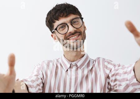 Headshot von zufrieden und nette gut aussehende glücklich kaukasischen Kerl bärtigen mit modischer Frisur in kühlen trendigen gestreiften Hemd ziehen Hände towads Kamera als ob man selfie freudig lächelnd Stockfoto