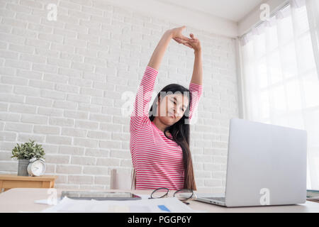 Asiatische Frau stretching arm, wenn auf dem Laptop an der weißen Wand im Hause arbeiten. Arbeit zu Hause Konzept. Entspannen Sie nach harter Arbeit Stockfoto