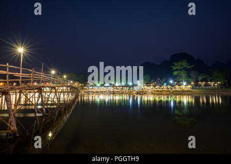 Reflexionen der Holzbrücke und Waterfront Restaurant durch den Fluss Nam Song in Vang Vieng, Vientiane, Laos, Provinz in der Nacht beleuchtet. Kopieren Sie Platz. Stockfoto