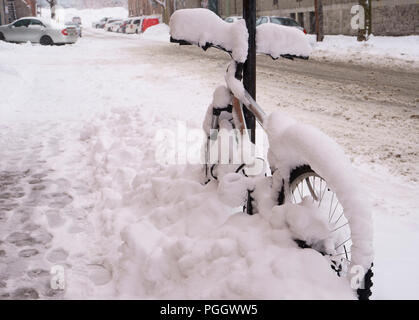 Der erste Schnee hat sich auf alles, was während der Nacht gefallen. Ein Fahrrad, auf dem Bürgersteig, ist wi Schnee bedeckt. Parkende Autos im Hintergrund. Stockfoto