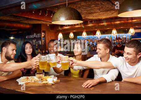 Lächelnd Gruppe von Freunden Bier an Design Pub genießen, Toasten und zu lachen. Schöne junge Menschen gemeinsam Spaß zu haben, Bier, das klirren Gläser Stockfoto