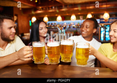 Vier Freunde Toasten mit Gläser helles Bier im Pub. Gruppe Leute Bier trinken, sich gemeinsam amüsiert, die Bier anstoßen Tabelle oben Stockfoto