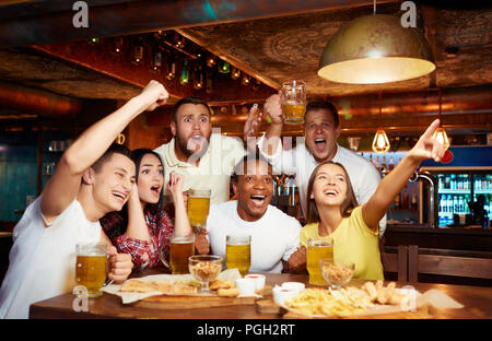 Gerne Freunde Spaß haben im Pub beobachten Sport im TV zusammen, trinken Bier, Jubel für die Mannschaft. Gruppe von Menschen feiern Sieg der Lieblingsmannschaft, Stockfoto