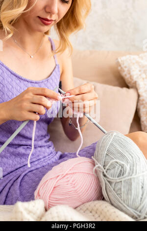 Nahaufnahme der Frau in einem lila Home Kleid strickt Ein hellrosa Schal oder Plaid aus natürlichen Threads auf dem Bett. Close-up horizontale Foto. Freiberufliche creati Stockfoto