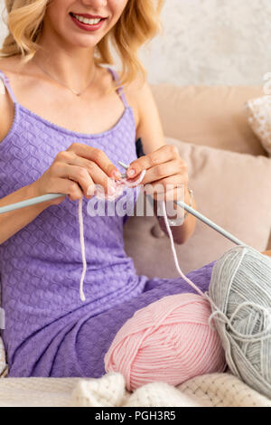 Nahaufnahme der Frau in einem lila Home Kleid strickt Ein hellrosa Schal oder Plaid aus natürlichen Threads auf dem Bett. Close-up horizontale Foto. Freiberufliche creati Stockfoto
