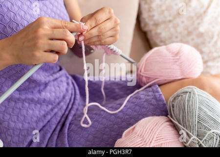 Nahaufnahme der Frau in einem lila Home Kleid strickt Ein hellrosa Schal oder Plaid aus natürlichen Threads auf dem Bett. Close-up horizontale Foto. Freiberufliche creati Stockfoto