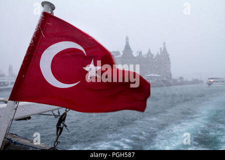 Türkische Flagge auf einem Schiff während eines Schneesturmes, eine Fähre zwischen Europa und Asien im Hintergrund gesehen werden kann, sowie den Bahnhof Haydarpasa Bild von Stockfoto