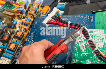 Entsorgung von e-Müll. Hand mit einer Zange. Stecker mit Kabel für Computer Mainboard. Leiterplatten, elektrische PC Teile auf farbigen Hintergrund. Stockfoto