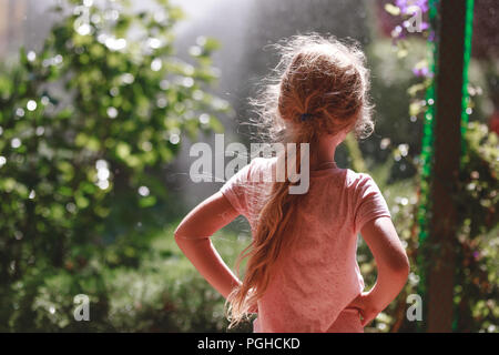 Zurück Blick auf sieben Jahre alt, blonde Mädchen mit Schlafanzug ständigen Outdoor im heimischen Garten in den frühen Morgen. Stockfoto