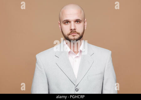 Portrait von Stattlichen traurige Verzweiflung im mittleren Alter kahl bärtigen Geschäftsmann in Classic Light grauen Anzug stehen, zu Kamera suchen mit gedrückter Gesicht. indo Stockfoto