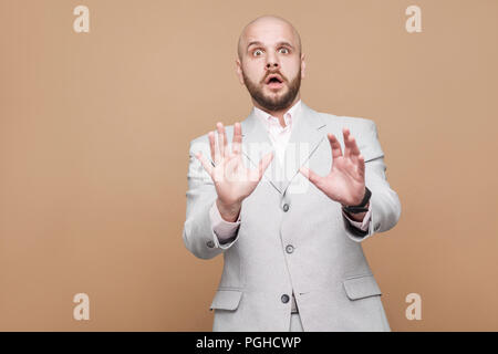 Portrait von mittleren Alters kahlen bärtigen Geschäftsmann in Classic Light grauen Anzug stehen und an der Kamera mit entsetzten Gesicht erschrocken betont. indoor s Stockfoto