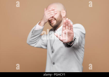 Hör auf, Ich will es sehen. Portrait von verwirrt im mittleren Alter kahl bärtigen Geschäftsmann in Classic Light grauen Anzug mit stop Geste, Abdeckung Stockfoto