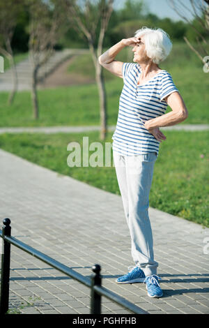 Volle Länge Portrait von Active Senior Frau weg suchen Abschirmung Augen aus Sonnenlicht im Freien Platz kopieren Stockfoto