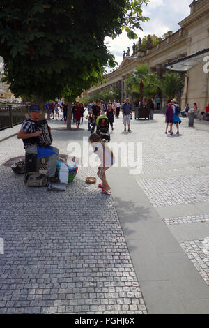 Junge Mädchen Geld zu geben, ein Straßenmusikant spielt Akkordeon auf der Straße in der Kurstadt Karlovy Vary, Westböhmen in Tschechien Stockfoto