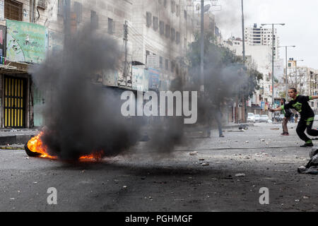 Hebron, Palästina, November 29, 2013: Junge Palästinenser, der sich hinter dem Rauch des brennenden Reifen während der Ausschreitungen in der Altstadt von Hebron. Stockfoto