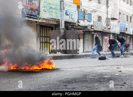 Hebron, Palästina, November 29, 2013: Junge Palästinenser sind versteckt hinter einer Board und ein Rauch des brennenden Reifen während der Ausschreitungen in der Altstadt von Hebron. Stockfoto