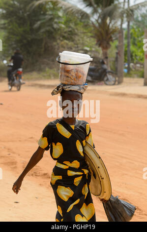 OUIDAH, BENIN - Jan 10, 2017: Unbekannter Beninischen jungen Mädchen in bunten Kleid trägt einen Eimer auf dem Kopf. Benin Kinder leiden der Armut aufgrund Stockfoto