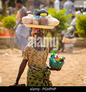 OUIDAH, BENIN - Jan 10, 2017: Unbekannter beninischen Frau trägt ein Becken auf dem Kopf und einem hölzernen Stuhl am Voodoo Festival, das jährlich ist Cele Stockfoto