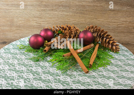 Drei weiße Tannenzapfen auf einem Bett aus Zeder und Balsam verzweigten, mit sechs Gold Zweig, Bälle, drei rote Ornamente und fünf Zimtstangen Stockfoto