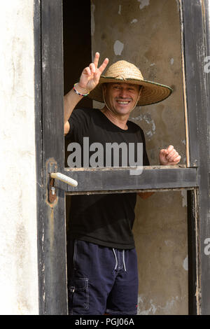 ELMINA, GHANA - Jan 18, 2017: Unbekannte europäische Tourist in einen Hut zeigt zwei Finger und lächelt in Elmina. Stockfoto