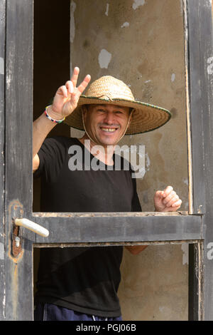 ELMINA, GHANA - Jan 18, 2017: Unbekannte europäische Tourist in einen Hut zeigt zwei Finger und lächelt in Elmina. Stockfoto