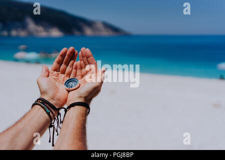 Offene Hand Palmen holding Metall Kompass gegen Sandstrand und das blaue Meer. Suchen Sie ihren Weg Konzept. Point of View pov Stockfoto