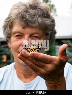 Ein älterer Frauen ein frisch aufgetaucht bewundern, Monarch butterfly, danaus Plexippus, sitzen auf ihrer Hand in einem Garten in Spekulant, NY, USA Stockfoto