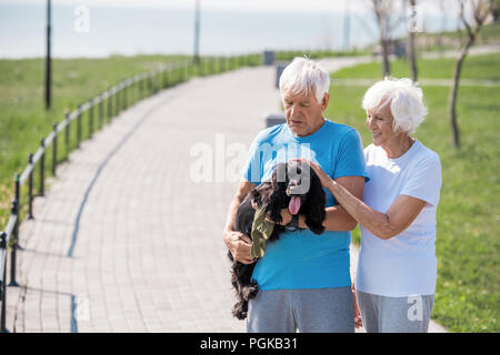 Portrait von Active Senior Paar liebevoll Streichelzoo Hund beim genießen Spaziergang im Park, Kopie Raum Stockfoto