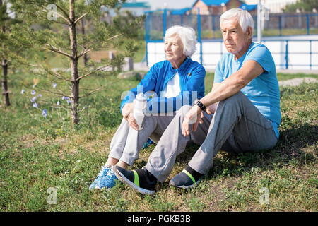 Portrait des modernen senior Paar sitzt auf Rasen durch Baum und genießen Sie sonniger Tag im Park zusammen, Kopieren Raum Stockfoto