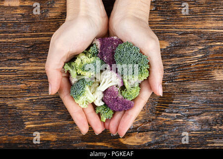 Blütenstände von bunten Blumenkohl - Weiß und Violett und Brokkoli in die Hände eines Mädchens auf einer hölzernen Hintergrund Stockfoto