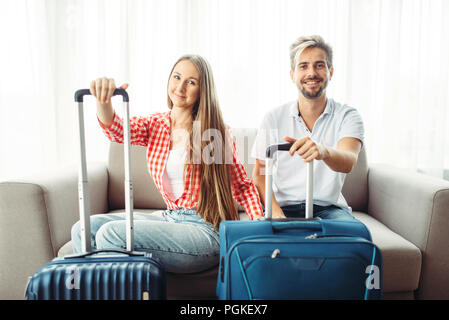 Junges Paar mit Koffern sitzen auf der Couch. Die Gebühren für die Reise. Gepäck Vorbereitung. Reisen und Tourismus Stockfoto