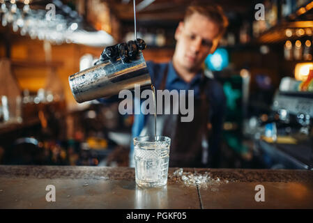 Männliche Barkeeper Schürze gießt einen Drink in ein Glas. Der Barkeeper an der Theke. Alkohol Getränke Vorbereitung Stockfoto