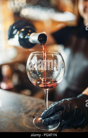 Weibliche Barkeeper Hände in Handschuhe gießt Rotwein in ein Glas. Frau Barkeeper an der Theke im Pub. Barkeeper Besetzung Stockfoto