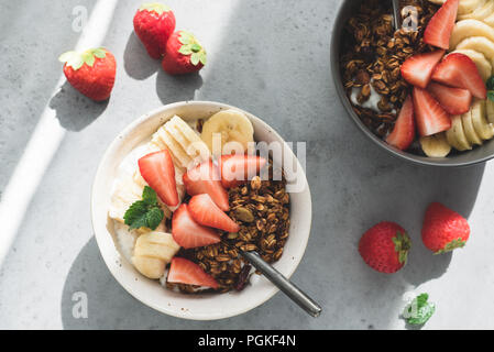 Chia pudding gekrönt mit Müsli und Obst in Schüssel auf grauem Beton Hintergrund. Ansicht von oben. Morgen Sonnenlicht Stockfoto