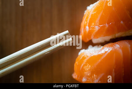 Verfügbare Bambus Stäbchen und Lachs sushi Close-up auf hölzernen Hintergrund Stockfoto