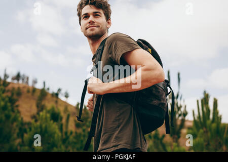 Menschen wandern in ländlicher Umgebung. Seitliche Sicht auf ein Mann mit einem Beutel zu Fuß durch den Wald. Stockfoto