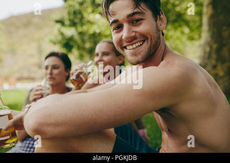 Freunde genießen Sie Urlaub in einem Park mit Getränken. Mann mit zwei weiblichen Freunde sitzen draußen Bier trinken. Stockfoto