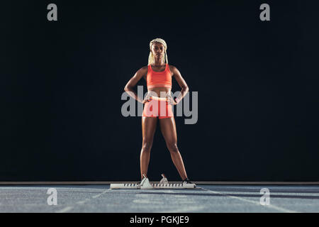 Weibliche sprinter stand neben einem Block auf der Laufstrecke auf schwarzem Hintergrund. Weibliche Läufer an der Startlinie auf einer all-Wetter ru Stockfoto