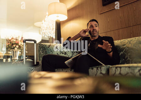 Reifen Geschäftsmann in der Lobby sitzen und Gespräch am Handy. Geschäftsmann auf wartet im Hotel Foyer, Anruf. Stockfoto