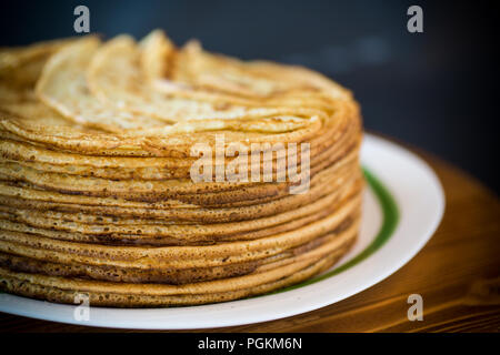 Große hohe dünne Pfannkuchen in einer Platte auf einem schwarzen Hintergrund Stapel Stockfoto