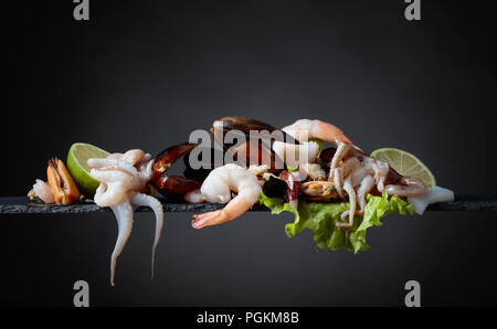 Köstliche Meeresfrüchte mit Salat und Kalk Schichten auf einem schwarzen Hintergrund gemischt. Stockfoto