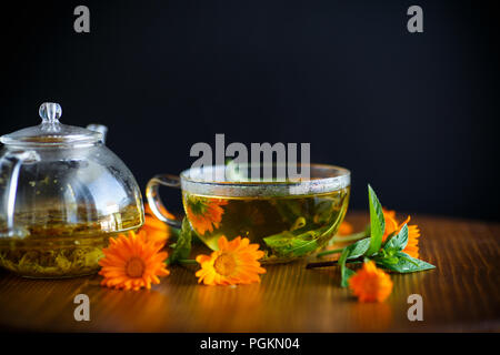 Frischen heißen Tee mit Kräutern und Ringelblume Blumen in einem Glas Schale auf einem Holztisch Stockfoto