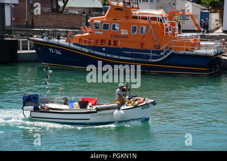 Ein Fischer in einem kleinen Boot in Weymouth Hafen an ein Rettungsboot. Weymouth, Jurassic Coast, Dorset, Großbritannien Stockfoto