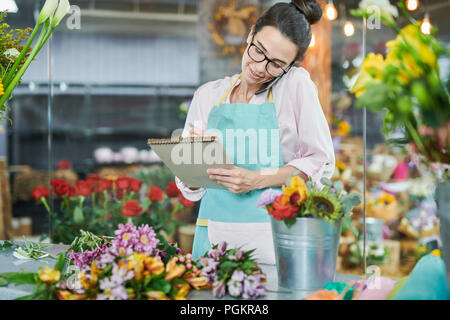 Porträt der jungen Frau, um durch Smartphone in Flower Shop Stockfoto