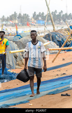 ELMINA, GHANA - Jan 18, 2017: Unbekannter ghanaischen Mann Spaziergänge auf dem Fischernetz in Elmina Port mit einem Eimer. Menschen in Ghana Leiden der Armut durch t Stockfoto