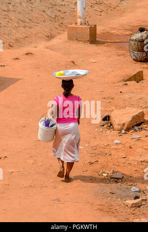 ELMINA, GHANA - Jan 18, 2017: Unbekannter ghanaischen Frau trägt ein Becken auf dem Kopf an der Küste von Elmina. Menschen in Ghana Leiden der Armut aufgrund Stockfoto