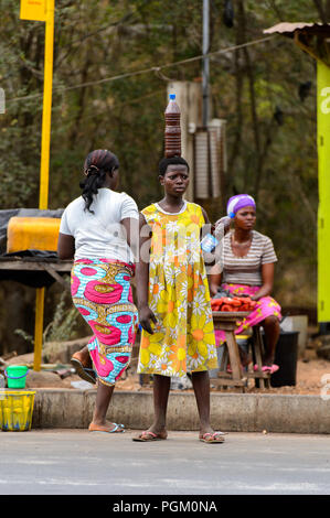PIRA, BENIN - Jan 12, 2017: Unbekannter beninischen Frau im gelben Kleid mit Blumen hält eine Flasche mit Flüssigkeit. Benin Menschen leiden unter der Armut aufgrund Stockfoto