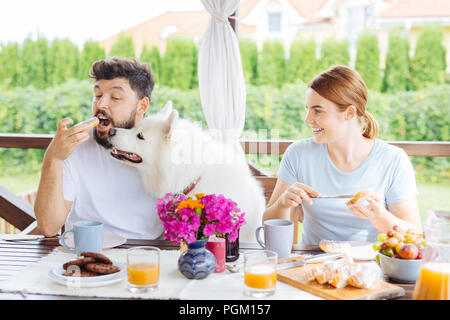 Glückliches Paar, das Frühstück auf der Sommerterrasse mit ihrem Hund Stockfoto