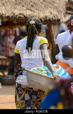 BOHICON, BENIN - Jan 12, 2017: Unbekannter beninischen Frau mit Zöpfe trägt ein Becken auf dem lokalen Markt. Benin Menschen leiden unter der Armut aufgrund der Stockfoto