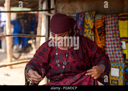 BOHICON, BENIN - Jan 12, 2017: Unbekannter beninischen Frau in Burgund Kleid trägt, Halskette und Kopftuch auf dem lokalen Markt. Benin Leute leiden von Stockfoto